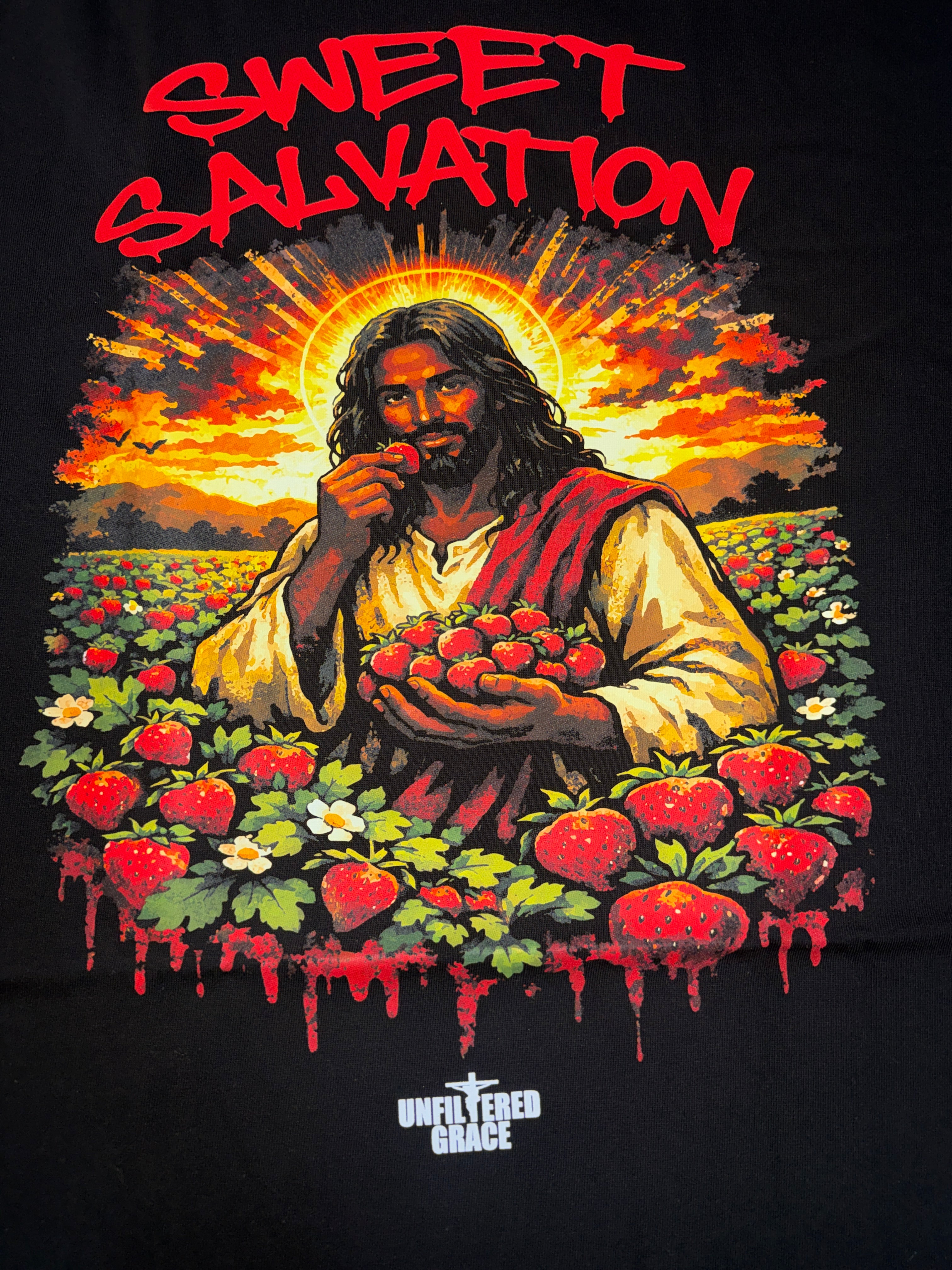 Black t-shirt design with Jesus holding strawberries in a field, titled 'Sweet Salvation'.